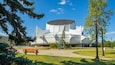 Ein modernes architektonisches Gebäude mit einem markanten, kreisförmigen Design, umgeben von einem gepflegten Park mit einer Bank und Bäumen.