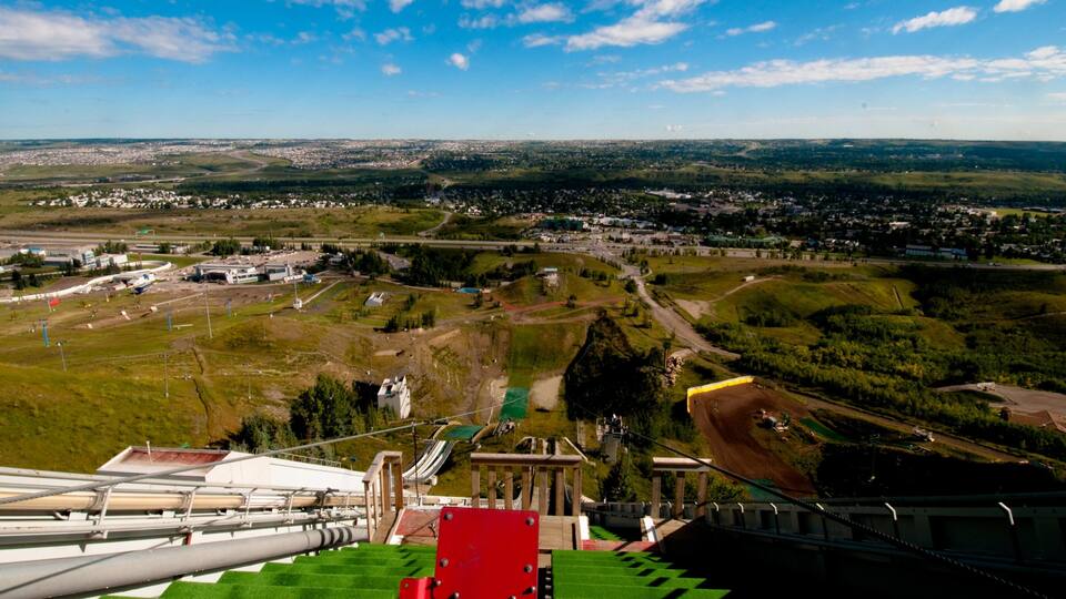 A panoramic view of a town with a large green park, a river, and a distant city skyline.