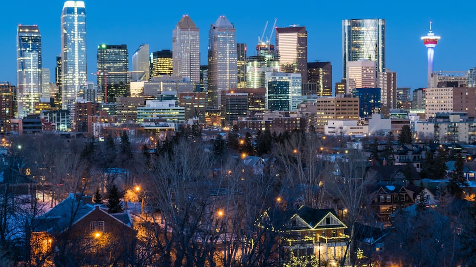 A city skyline with modern buildings, a prominent tower, and a well-lit house in the foreground.