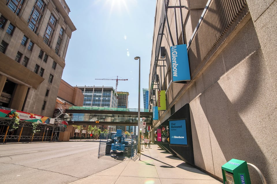 A city street with a construction crane, a pedestrian crossing, and storefronts including a Glenbow store.