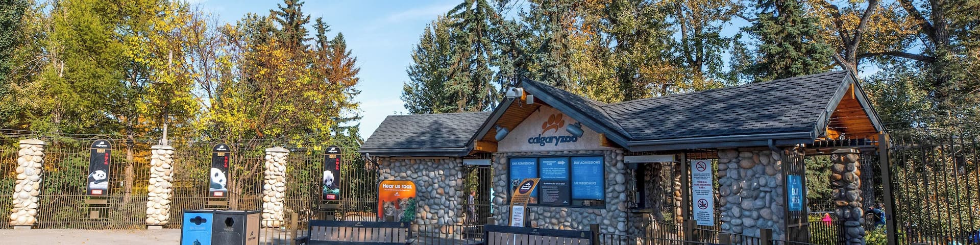 A stone building with a sign reading "cayuga zoo" surrounded by benches and a stone fence.
