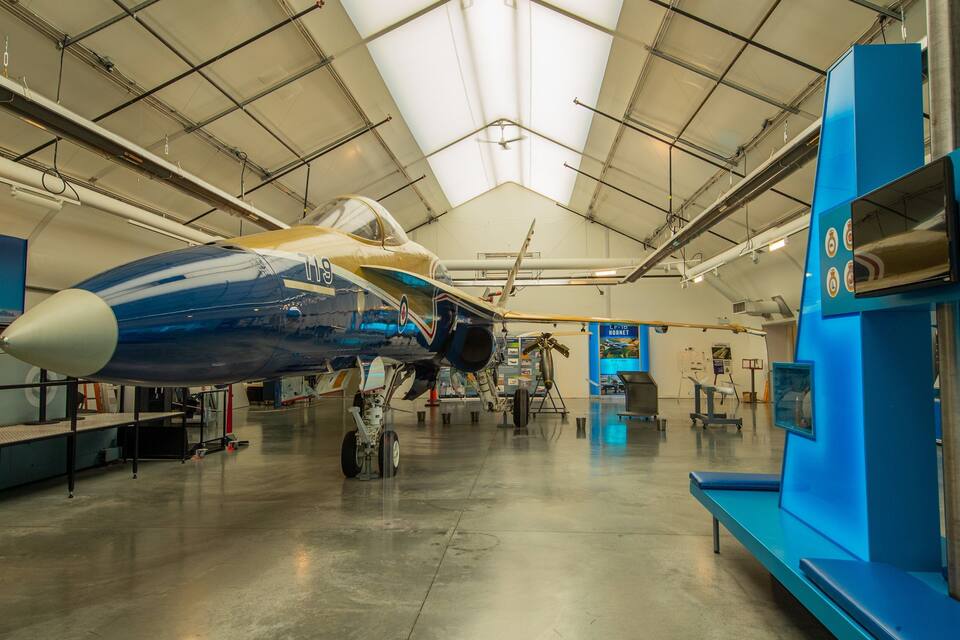 A blue and white vintage aircraft in a museum hangar with informational displays.