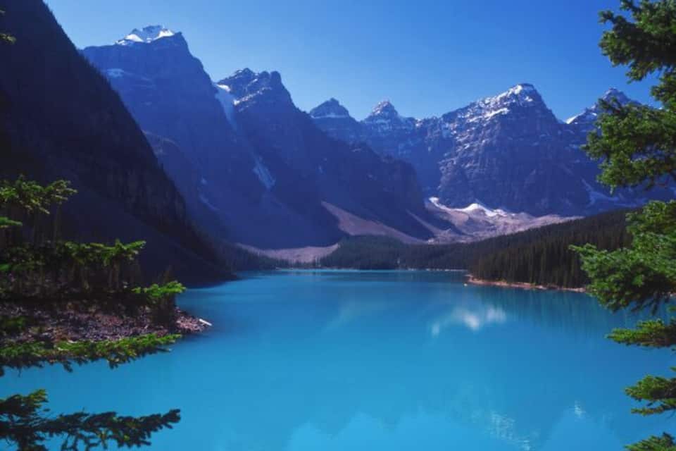 Un lago turquesa rodeado de montañas y un bosque denso.