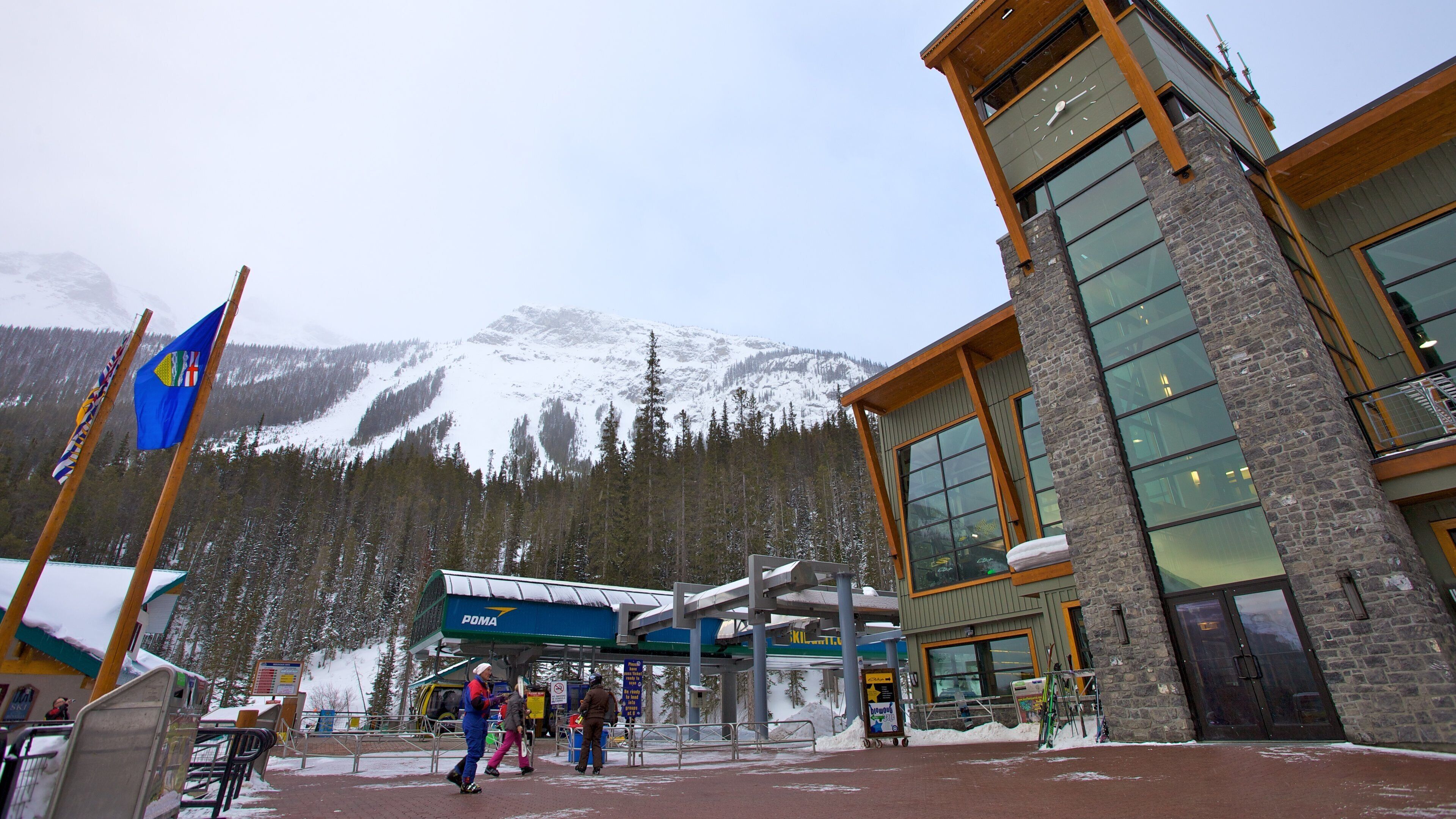 A ski resort entrance with a mountain backdrop, a building with large windows, and flags.