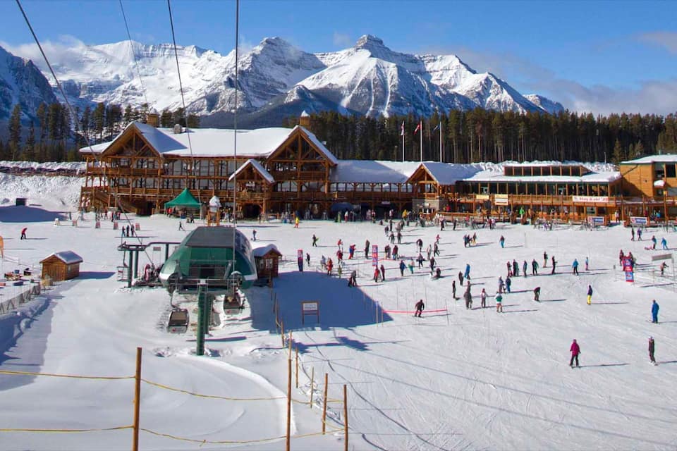 A snow-covered ski resort with wooden lodges, a ski lift, and a mountainous backdrop.