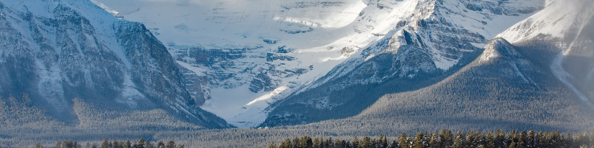 A snow-covered mountain lodge with a ski slope in the foreground and a forested valley in the background.