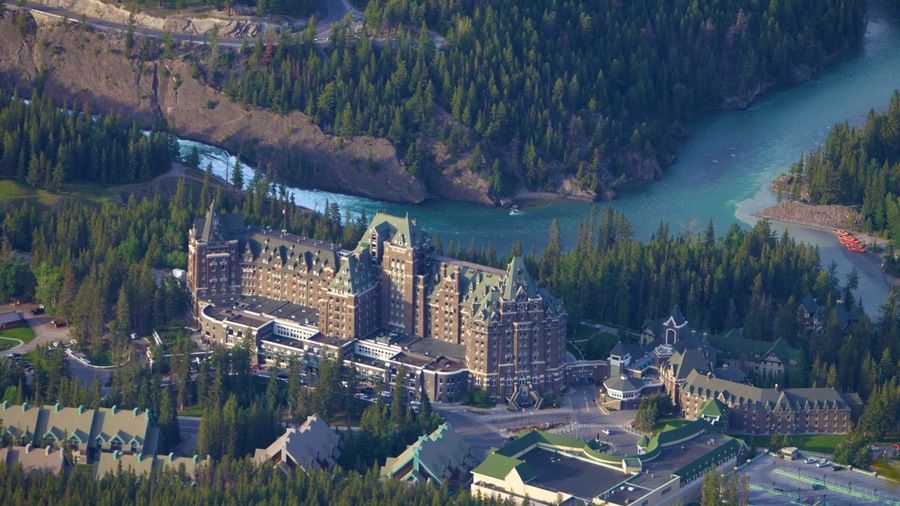 A large, historic building complex surrounded by dense forests and a river.