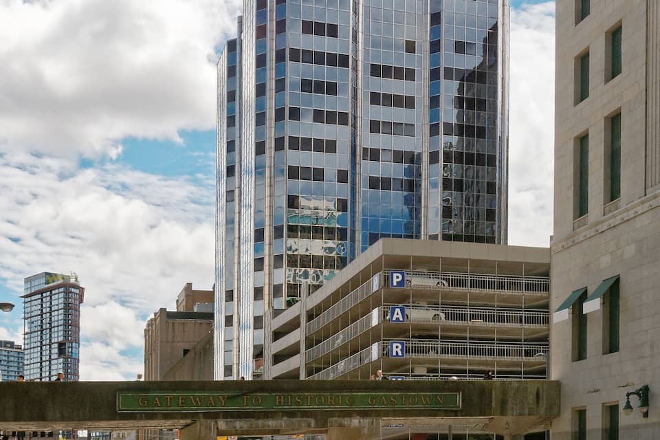 A city street with a modern building, a parking garage, and a sign reading "Gateway to History Gastown."