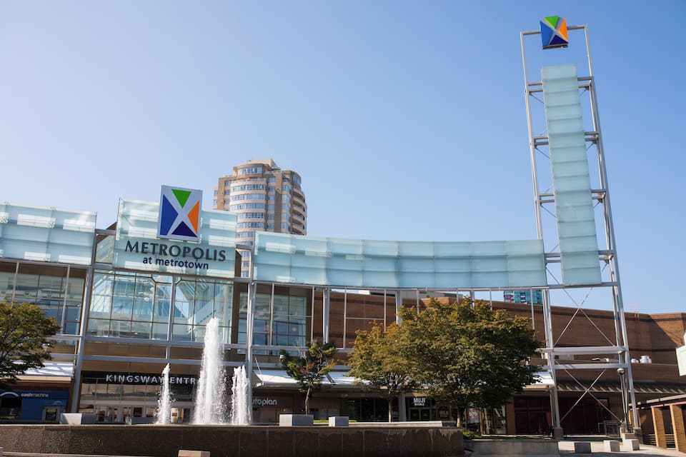 A modern building with a glass facade, a fountain, and a tall structure with a flag.