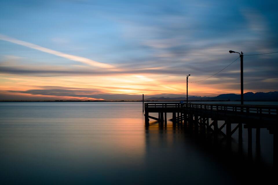 A pier extending into calm water during sunset with a clear sky.