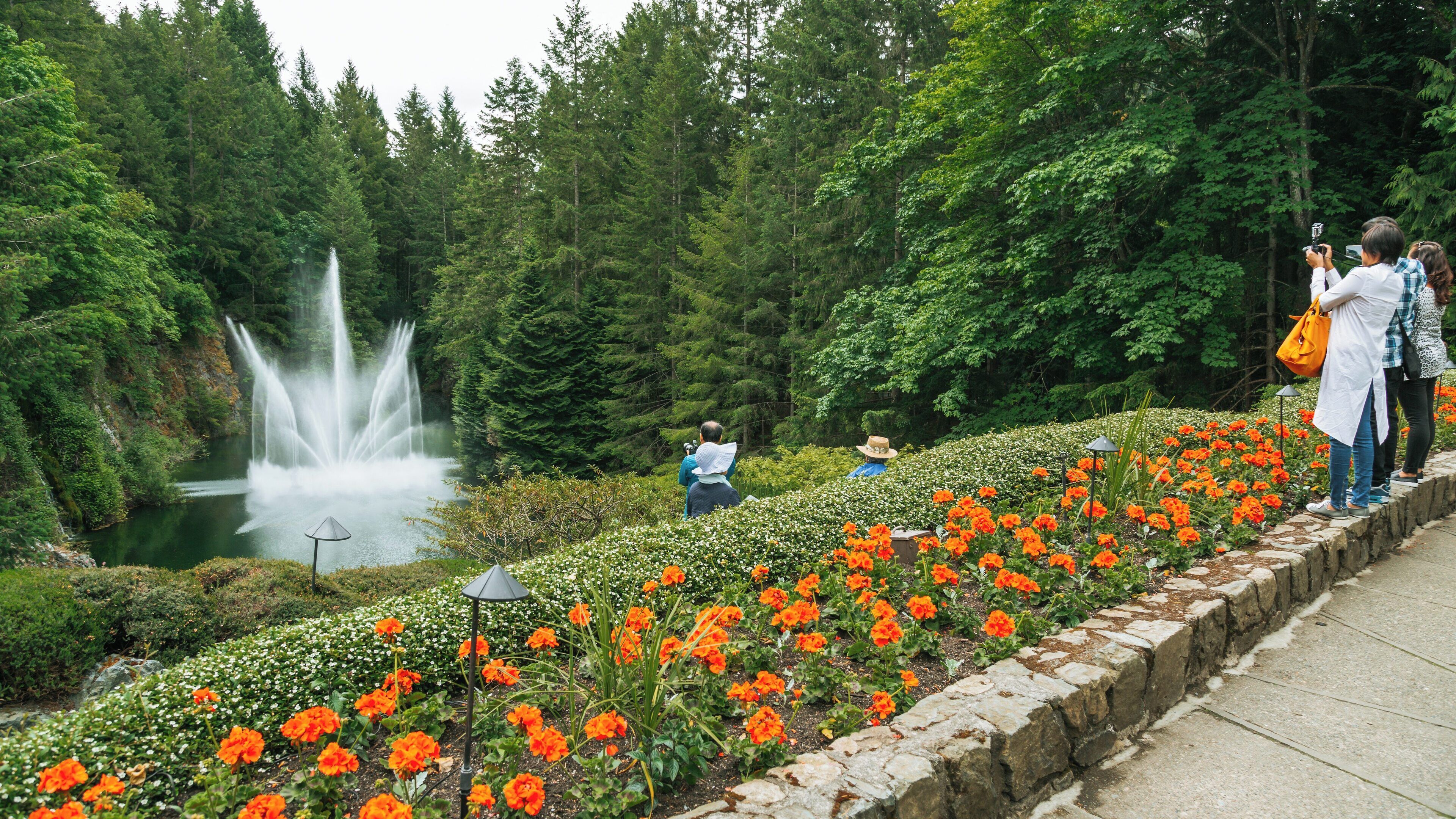 Visitors capture moments by the vibrant flowers in Butchart Gardens, surrounded by lush greenery and a stunning fountain display in British Columbia