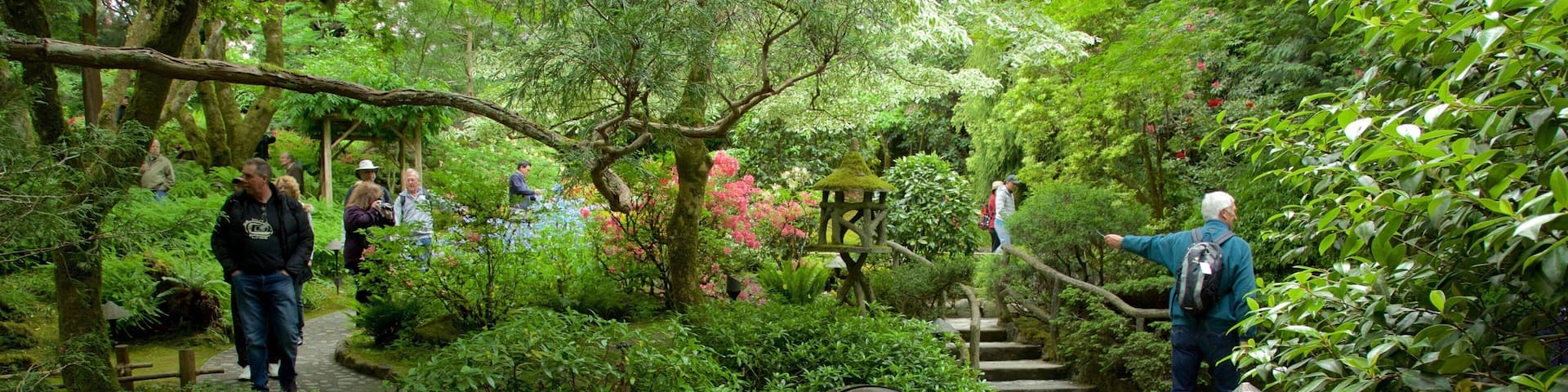 A red bridge in a lush garden with people walking around.