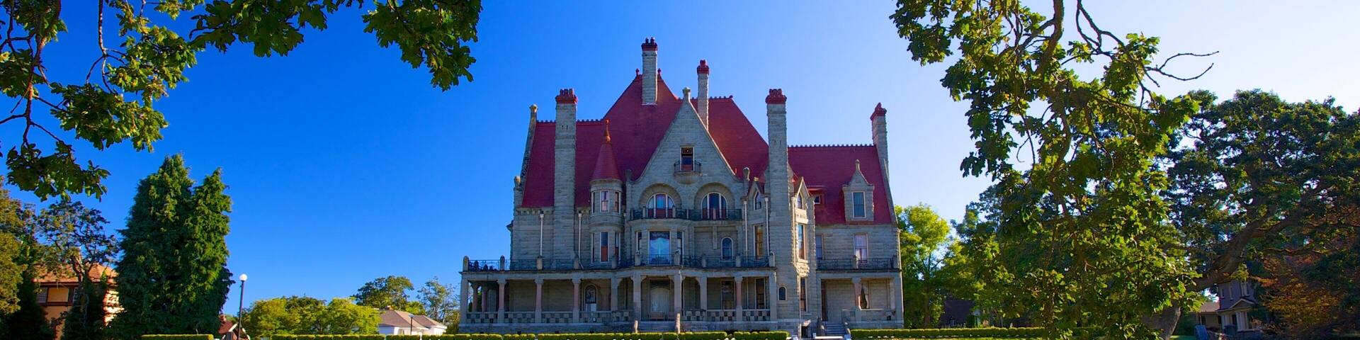 A large, historic mansion with a red roof and multiple chimneys, surrounded by a well-maintained lawn and a pathway leading to the entrance.