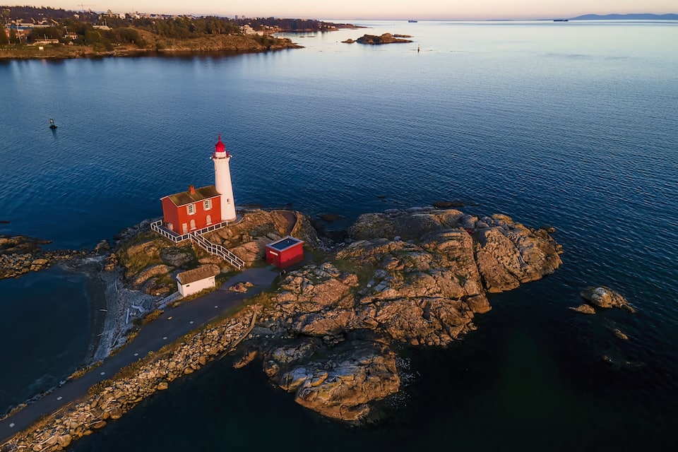 A lighthouse on a rocky island with a clear view of the surrounding water and distant land.