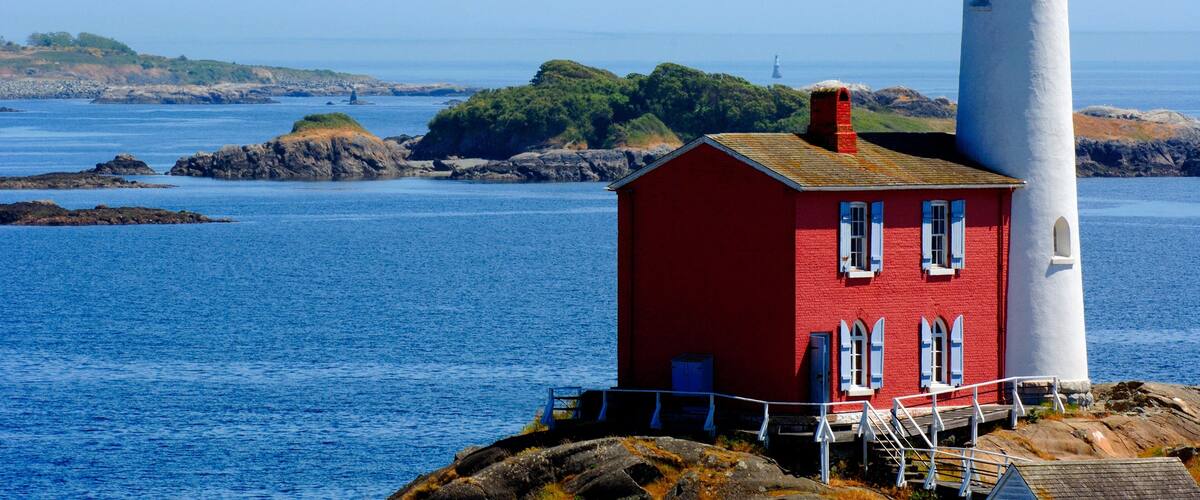 A red lighthouse with a white tower, surrounded by calm blue waters and rocky terrain.
