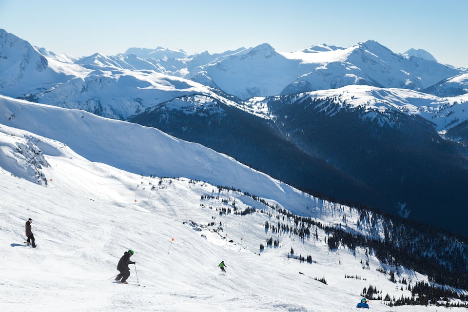 A snowy mountain landscape with skiers and a clear blue sky.