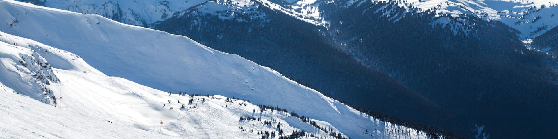 Skiers on a hill at the top of Blackcomb, 7th Heaven, with a view looking toward Whistler on a sunny day.