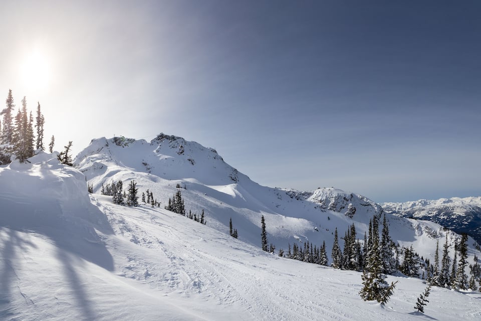 A snow-covered mountain landscape with a clear sky and sunlight.
