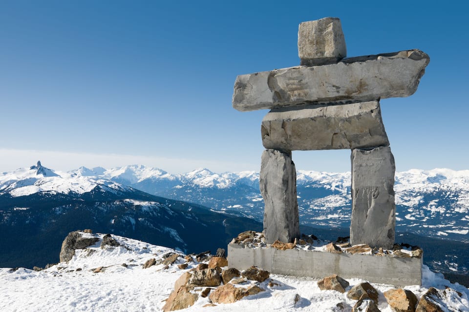 Un totém en la cima nevada de una montaña, con montañas cubiertas de nieve al fondo.