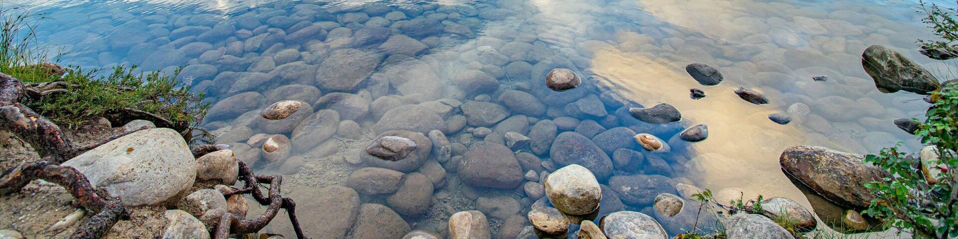 A clear lake with visible rocks and a mountain range in the background.