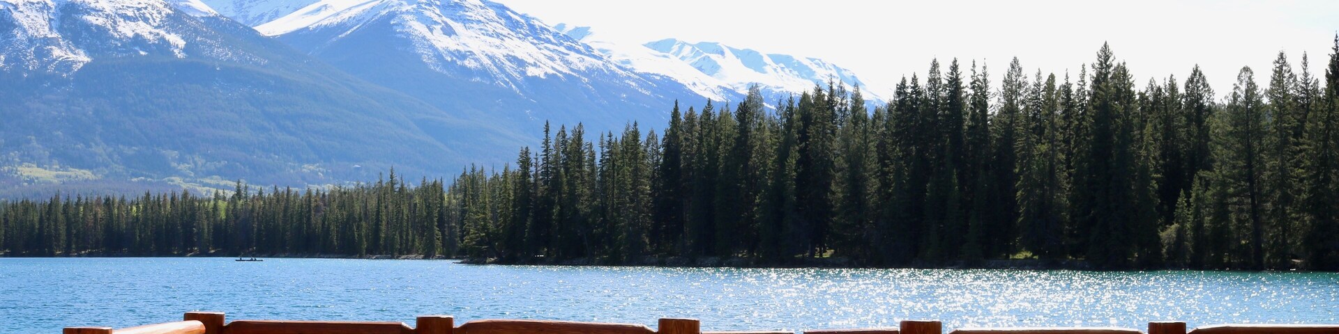 Terraza a orillas del lago con sillas de madera y vistas a montañas nevadas y un bosque denso.