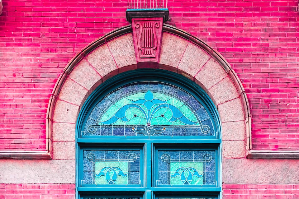 Ein rotes Backsteingebäude mit einem blauen, bogenförmigen Fenster mit aufwendigen Glasmalereien.
