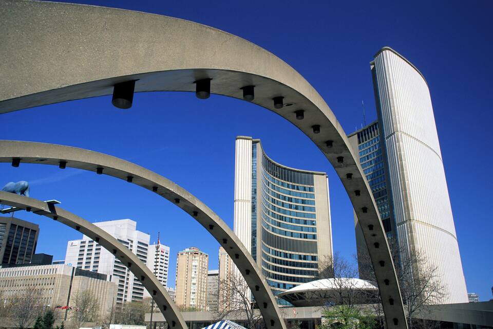 Un paisaje urbano moderno con una llamativa escultura metálica curva y edificios altos bajo un cielo azul despejado.