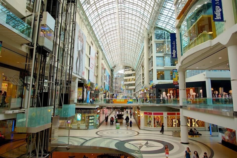 Um centro comercial com vários andares, teto de vidro, diversas lojas e um átrio central.