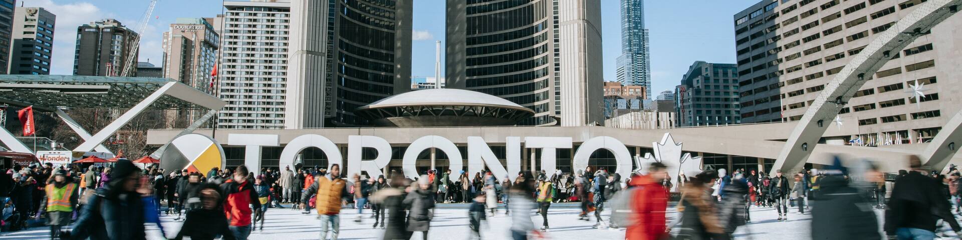 Nathan Phillips Square featuring signage and ice skating as well as a large group of people