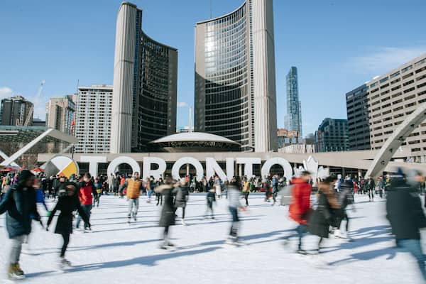Nathan Phillips Square featuring signage and ice skating as well as a large group of people
