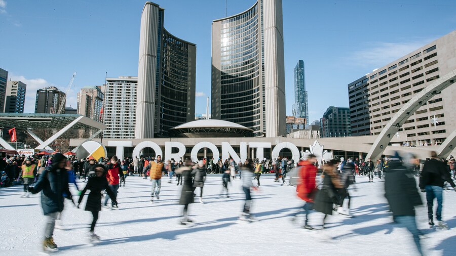 Nathan Phillips Square featuring signage and ice skating as well as a large group of people
