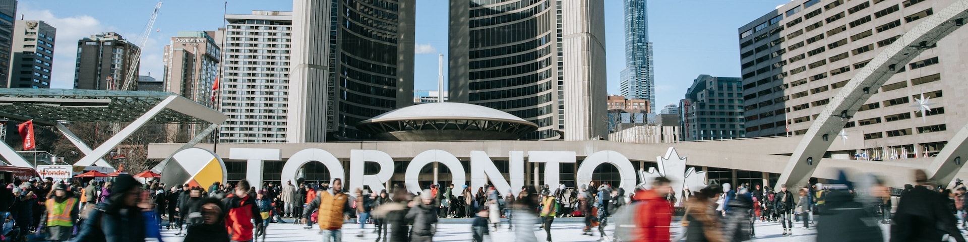 Nathan Phillips Square featuring signage and ice skating as well as a large group of people