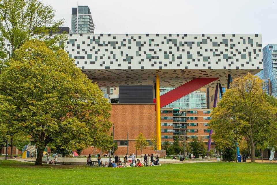 Un edificio moderno con una facciata pixelata, circondato da un parco con persone e alberi.