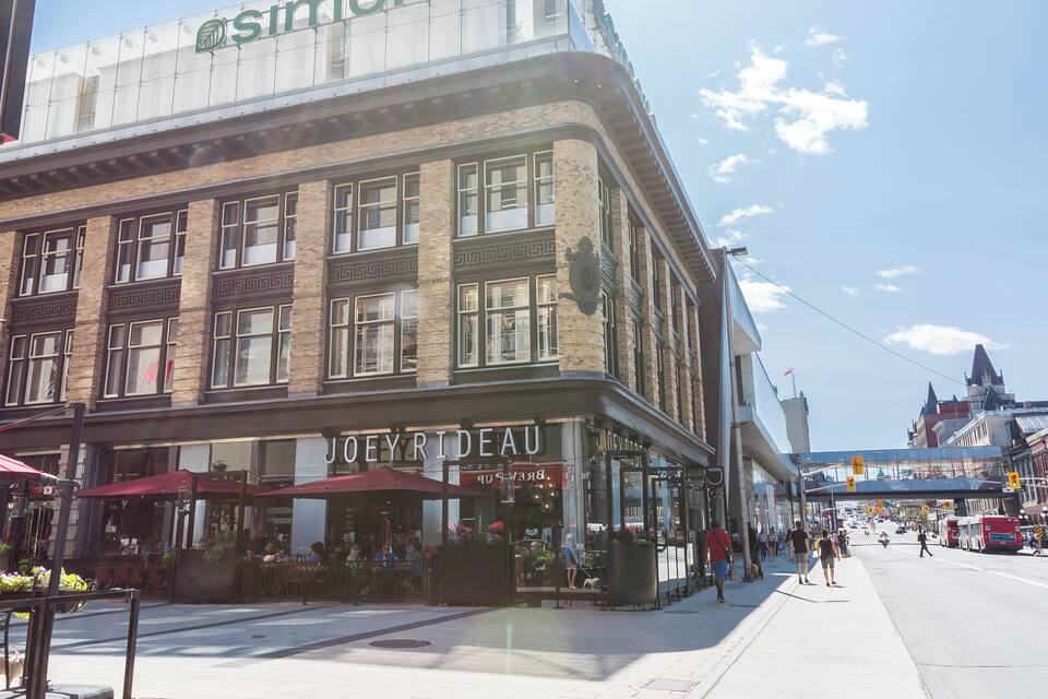 A street with a building labeled 'JOEY RIDEAU' and a clock tower in the background.