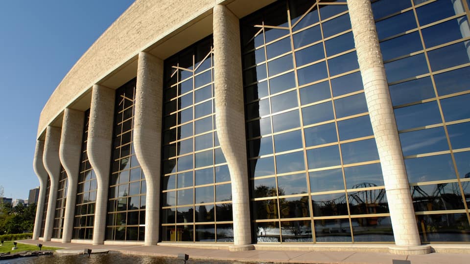 A modern building with a unique curved facade and large windows reflecting the sky and surrounding area.