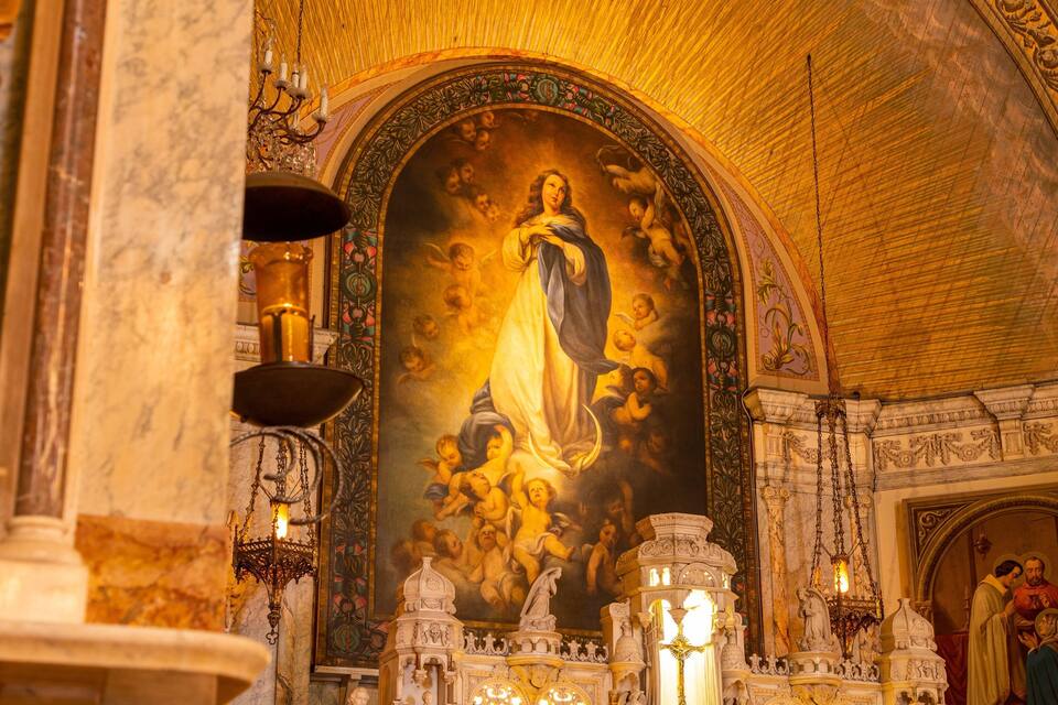 Interior de iglesia ricamente decorado, con un cuadro religioso central, techo intrincado y detalles arquitectónicos elaborados.
