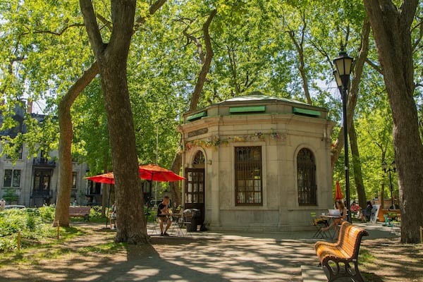Um parque com um coreto, guarda-sóis vermelhos e bancos.