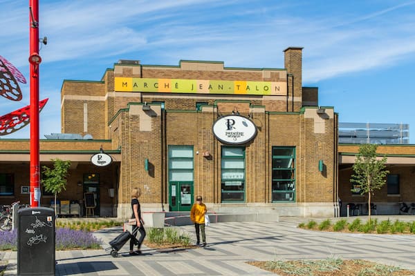 Un bâtiment en briques sur lequel on peut lire l’inscription « MARCHÉ JEAN-TALON » et une autre inscription indiquant « PREMIÈRE MOISSON ».