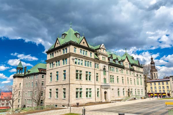 Un bâtiment historique doté de toits végétalisés et d’une tour, entouré d’un ciel dégagé et de quelques nuages.