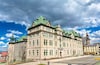 A historic building with green roofs and a tower, surrounded by a clear sky and a few clouds.