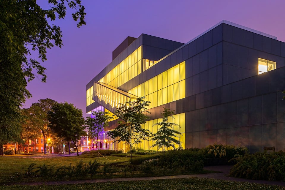 Un edificio moderno con ventanas amplias y fachada iluminada al anochecer.