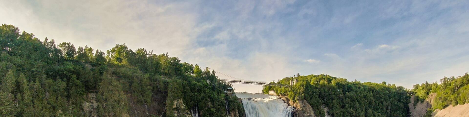 A waterfall cascading down a steep cliff surrounded by dense forest. A bridge spans the river below.