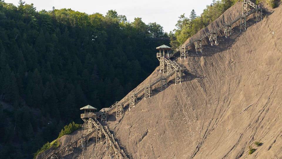A steep, rocky hillside with a series of wooden staircases leading up to a small gazebo-like structure.