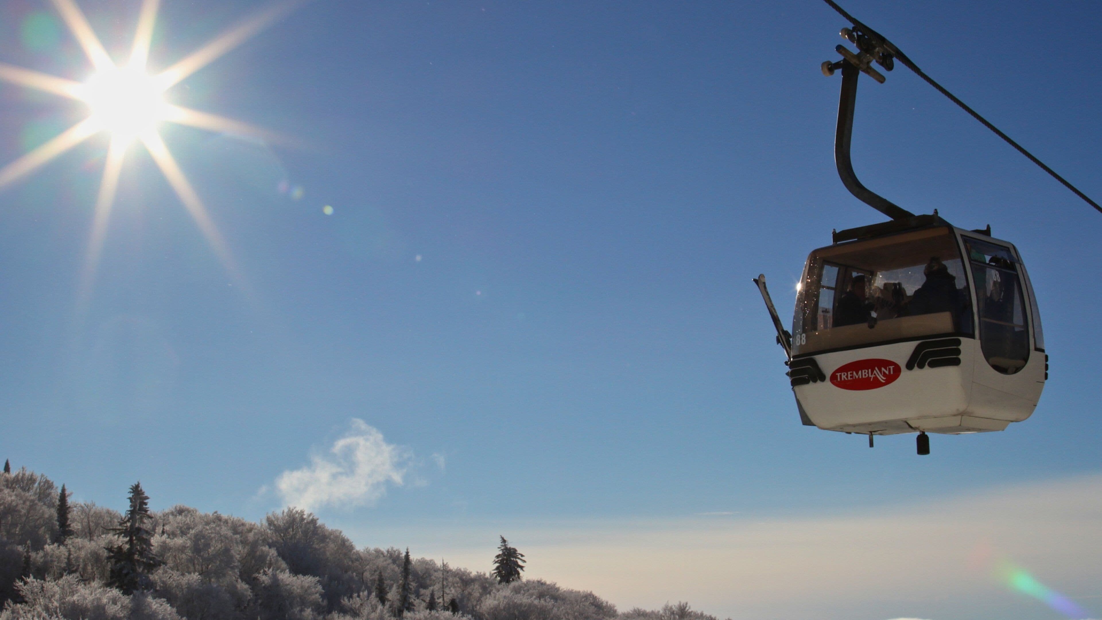 Un teleférico con el número 88 y la palabra TREMBLANT en su lateral, suspendido sobre un bosque nevado.