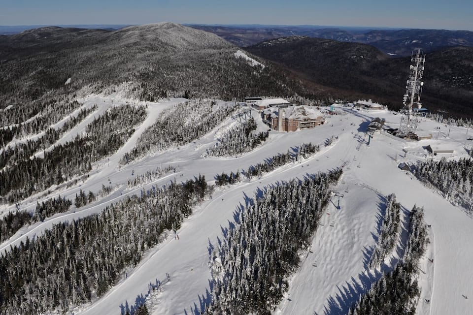 Un centro de esquí cubierto de nieve con telesillas, una cabaña y montañas al fondo.