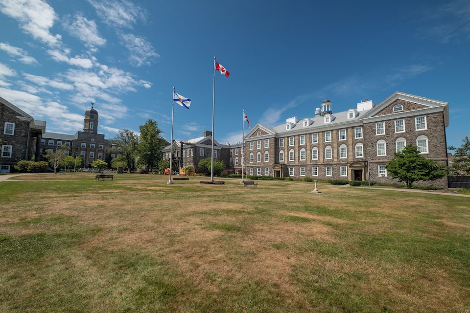 A large brick building with a clock tower, surrounded by a grassy field and several flags.