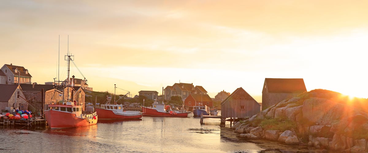 A harbor with boats, wooden buildings, and a sunset.