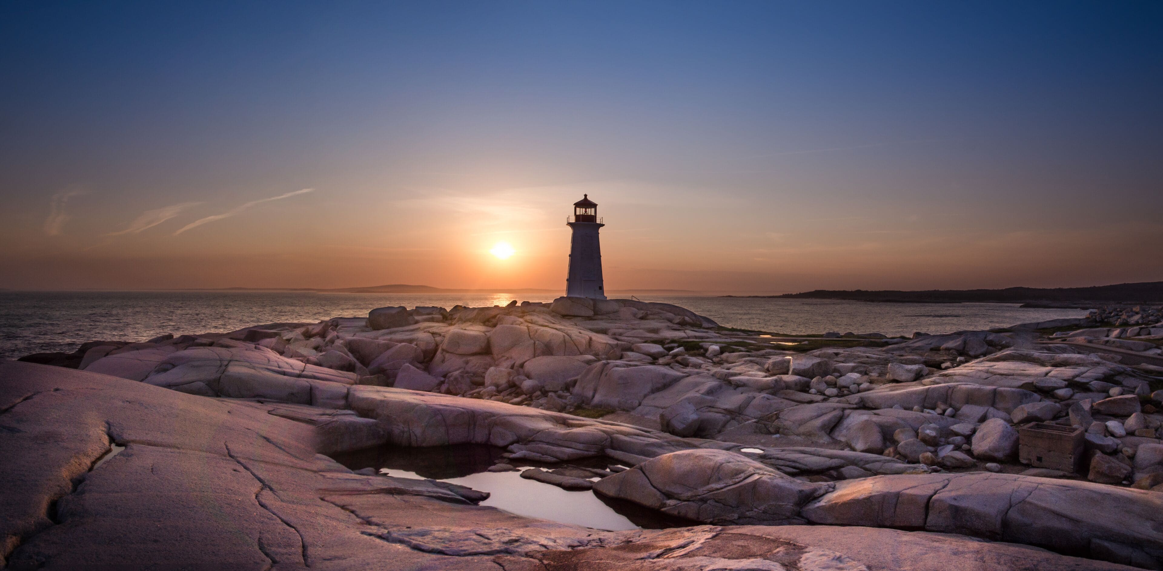 A lighthouse on rocky terrain at sunset.