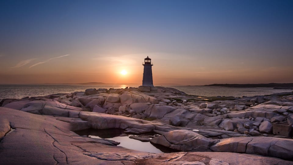 A lighthouse on rocky terrain at sunset.