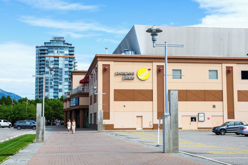 A building with a 'prospera place' sign, a parking lot, and a tall building in the background.
